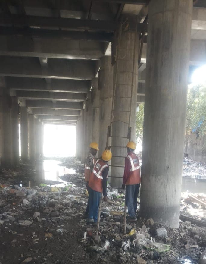 Site engineers inspecting a reinforced concrete column beneath the elevated treatment deck, above the cleared Poisar riverbed