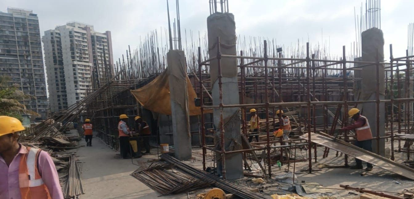 Column reinforcement and starter bars rising from the STP deck slab during construction, with Kandivali residential towers behind