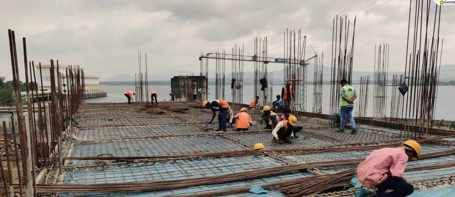 Workers tying reinforcement steel on a slab deck of the Bhama Askhed intake structure, the dam waters visible behind