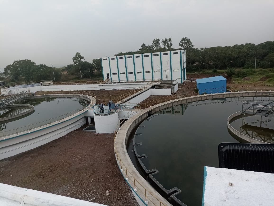 Paired circular clarifier units and the filter house building at the PCMC 100 MLD water treatment plant, with operators on the central walkway
